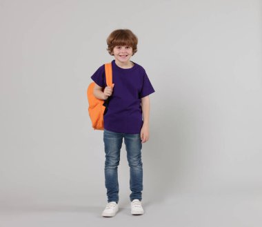 Açık gri arka planda sırt çantası olan sevimli bir okul çocuğu.