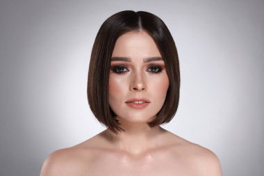 Açık gri arka planda muhteşem düz saçlı güzel bir genç kadının portresi.