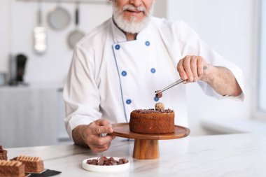 Yaşlı pasta şefi mutfaktaki masada lezzetli pastayı dekore ediyor, yakın plan.