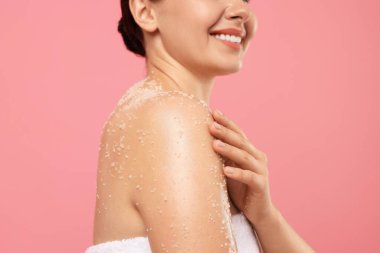 Gülümseyen kadın omuzlarını pembe arka planda ovalıyor, yakın plan.