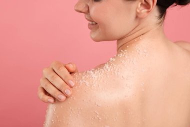 Gülümseyen kadın omuzlarını pembe arka planda ovalıyor.