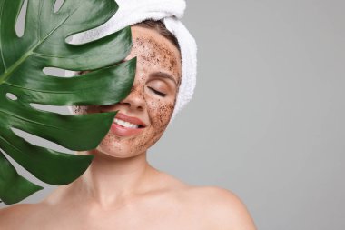 Yüzünde vücut fırçası ve gri arka planda canavar yaprağı olan gülümseyen bir kadın. Metin için boşluk