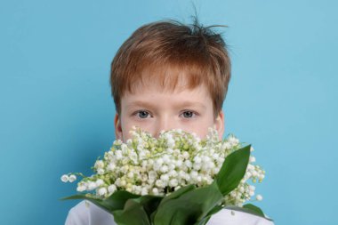 Açık mavi arka planda, vadideki güzel çiçekleri olan çocuk.