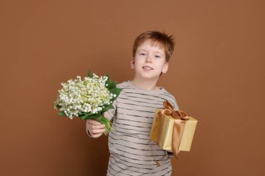 Elinde bir buket güzel çiçekli çocuk ve kahverengi arka planda bir hediye.