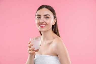 Pembe arka planda bir bardak kolajen suyu olan mutlu bir kadın.