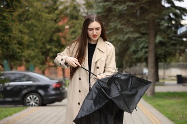 Parkta kırık şemsiyeli üzgün kadın