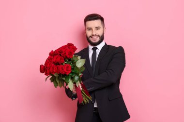 Pembe arka planda kırmızı güller açan mutlu bir adam.