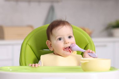 Evdeki beslenme sandalyesinde yemek yiyen şirin bir bebek.
