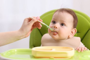 Anne bebeğini sandalyeyle besliyor, yakın plan.