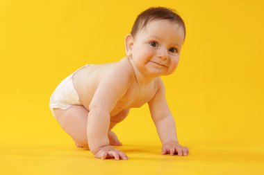 Sarı arka planda emekleyen sevimli küçük bebek.