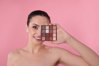 Gülümseyen kadın pembe arka planda göz farı paletiyle gözlerini kapatıyor.