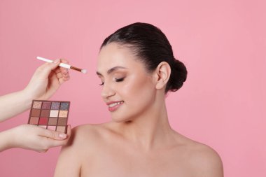 Makyaj sanatçısı pembe arka planda kadınların yüzüne göz farı uyguluyor.