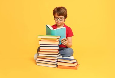 Turuncu arka plan hakkında çok farklı kitapları olan bir çocuk.