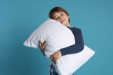 Açık mavi arka planda yastığı olan sevimli bir çocuk.