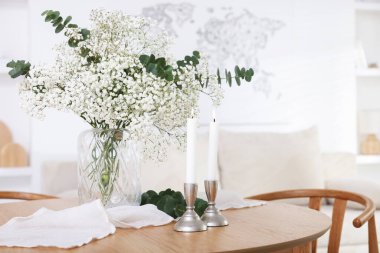 Vazoda okaliptüs dalları ve kapalı masa üzerinde mum yakan güzel çikila çiçekleri.