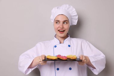 Üniformalı şekerci açık gri arka planda lezzetli ekinler tutuyor.