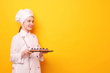 Üniformalı şekerlemeci turuncu arka planda lezzetli ekinler tutuyor, mesaj için yer var.