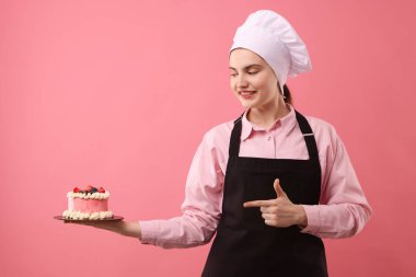 Şekerci pembe arka planda lezzetli bir pasta tutuyor.