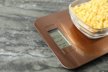 Modern elektronik mutfak terazisi, bir kase çiğ makarna ve gri mermer masa, yakın plan. Metin için boşluk