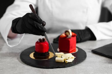 Mutfaktaki açık gri masada lezzetli bir tatlıyı dekore eden şekerci, yakın plan.