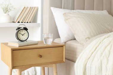 Alarmlı komodinli komodin, bir bardak su ve yatağın yanında kitap.