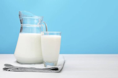 Bardakta taze süt ve açık mavi arka planda beyaz ahşap masada sürahi. Metin için boşluk
