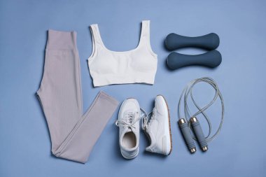 Spor kıyafetleri, spor ayakkabıları, ip atlama ve gri arka planda dambıllar, düz yatış.