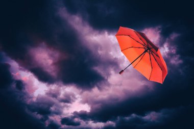 Koyu bulutlu gökyüzünde uçan kırmızı şemsiye. Fırtınalı hava