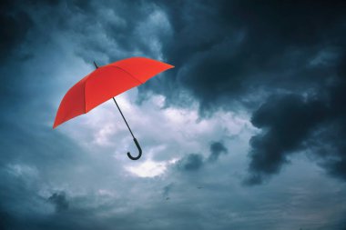 Koyu bulutlu gökyüzünde uçan kırmızı şemsiye. Fırtınalı hava