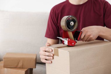Karton kutuyu kapalı bir yere kapatmak için yapıştırıcılı bant kullanan bir adam.