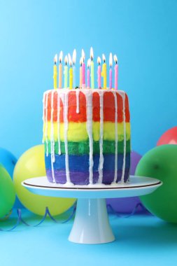 Nefis gökkuşağı pastası yanan mumlar ve açık mavi arka planda balonlar