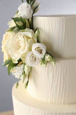 Gri arka planda çiçeklerle süslenmiş lezzetli düğün pastası, yakın plan.