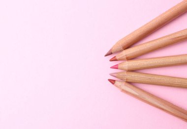 Açık pembe arka planda bir sürü farklı dudak kalemi, düz yatış. Metin için boşluk