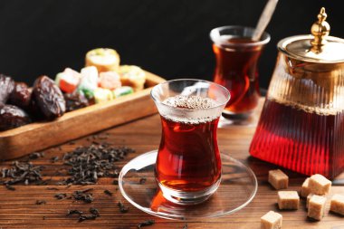 Geleneksel Türk çayı cam fincanlar, çaydanlık, kuru yapraklar, kahverengi şeker ve tatlılar ahşap masada, yakın plan