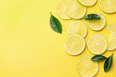 Dilimler taze limon ve yeşil yapraklar sarı arka planda, düz yerde. Metin için boşluk
