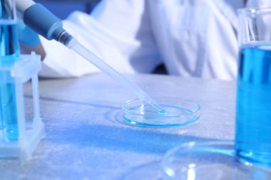 Bilimadamı laboratuardaki masada mikropipetle numune alıyor, yakın plan.