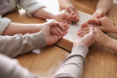 İncilli aile ahşap masada dua ediyor, yakın plan.