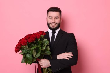 Pembe arka planda kırmızı güller açan mutlu bir adam.