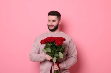 Pembe arka planda kırmızı gül buketi olan adam.