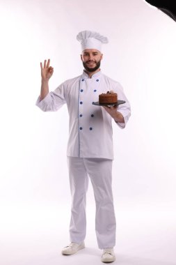 Üniformalı mutlu pastacı lezzetli çikolatalı pasta tutuyor ve beyaz arka planda güzel bir jest yapıyor.