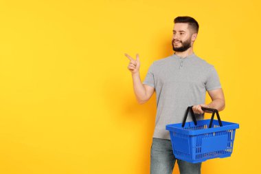 Boş alışveriş sepeti olan adam turuncu arka plandaki bir şeyi işaret ediyor, mesaj için boşluk.