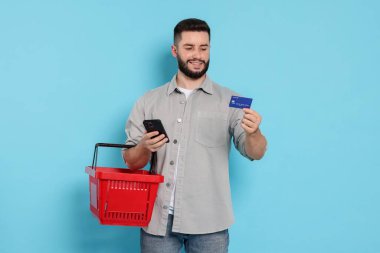 Açık mavi arka planda boş alışveriş sepeti ve kredi kartı olan bir adam.