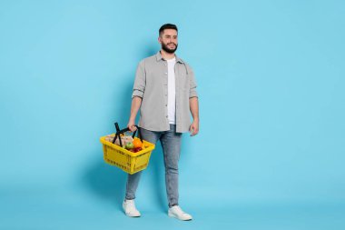 Açık mavi arka planda ürünlerle dolu alışveriş sepeti olan bir adam.