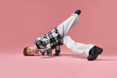 Kulaklıklı, şık elbiseli, pembe arka planda dans eden bir çocuk.