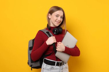 Sarı arka planda dizüstü bilgisayarı olan gülümseyen genç kız.