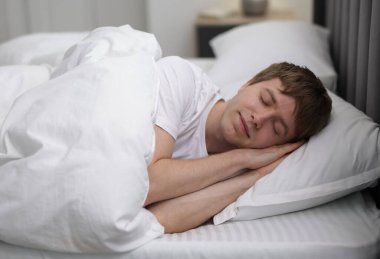 Genç adam yatağında uyuyor.