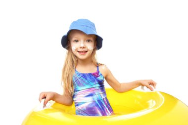 Cildinde güneş kremi ve beyaz arka planda şişme yüzük olan gülümseyen küçük bir kız.