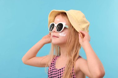 Yüzünde açık mavi arka planda güneş kremi olan sevimli küçük bir kız.