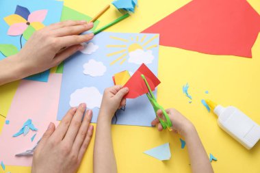 Anne ve kızı sarı masada el yapımı bir proje yapıyor.