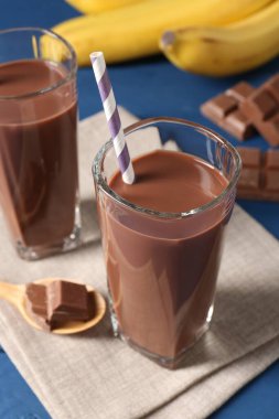 Lezzetli çikolatalı süt bardaklarda, parçalar ve muzlar mavi masada, yakın plan